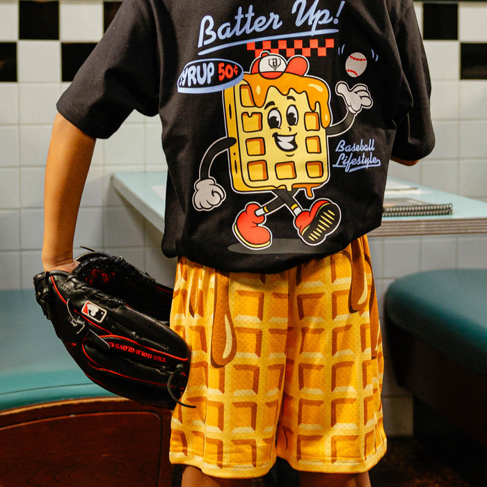Person wearing a black t-shirt with a cartoon waffle character and waffles shorts holding a baseball glove.