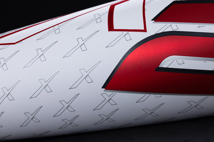 Close-up of a white surface with small gray X shapes and a large, glossy red character—reminiscent of the bold design on the Marucci 2025 CATX2 (-10) USSSA Baseball Bat: MSBCX210.
