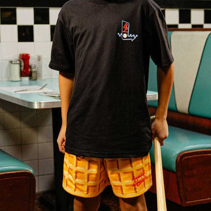 Person wearing a black t-shirt with a BL101 logo and waffle shorts in a retro diner setting