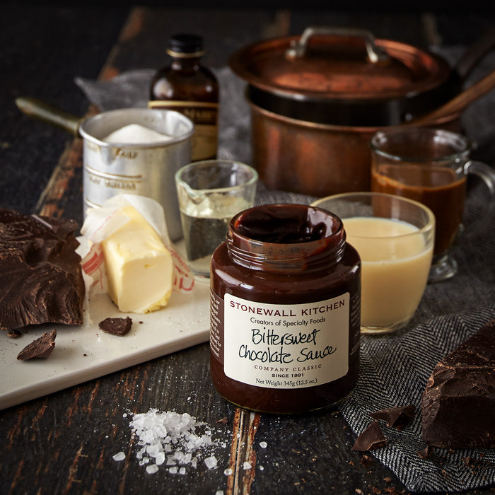 jar of stonewall kitchen bittersweet chocolate sauce with salt and chocolate and bottle of vanilla and copper pan