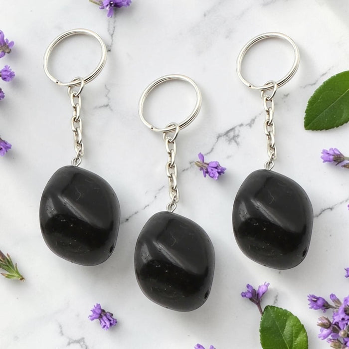 Three Black Obsidian keychains on a marble surface with purple flowers and green leaves.