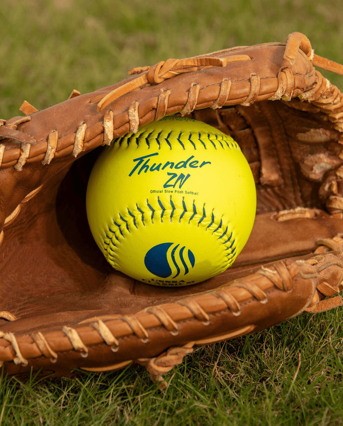 A baseball in a glove, much like the Dudley USSSA Thunder ZN Classic M 12" 40/325 Composite Slowpitch Softballs (4U540Y), is ready for play on the field.