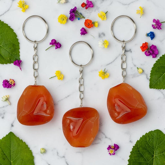 Three Carnelian keychains on a marble surface with flowers and leaves.