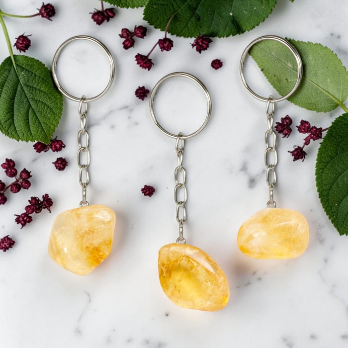 Three Citrine keychains on a marble surface with green leaves and red berries.