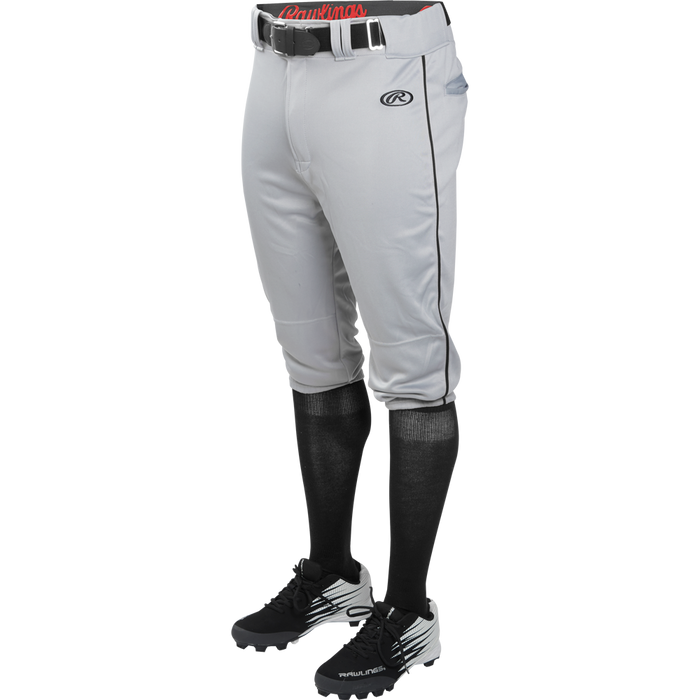 A person wears Rawlings Adult Launch Knicker Baseball Pants with black piping in Blue Grey/Black, featuring the Rawlings logo on the left thigh, paired with a black belt, black knee-high socks, and black cleats with white accents.