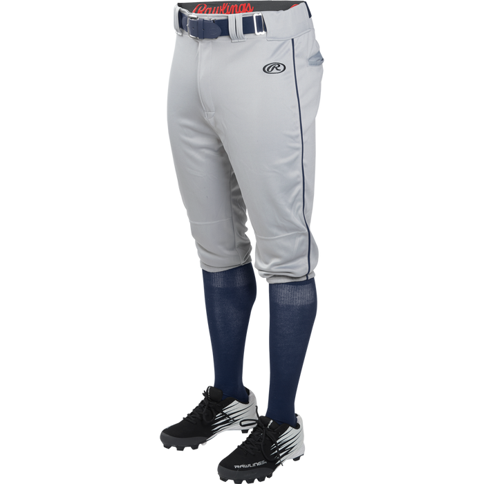 A person wears Rawlings Adult Launch Knicker Baseball Pants with Piping (Blue Grey/Navy), styled with a blue belt, blue knee-high socks, and black and white cleats, shown waist down against a plain background.