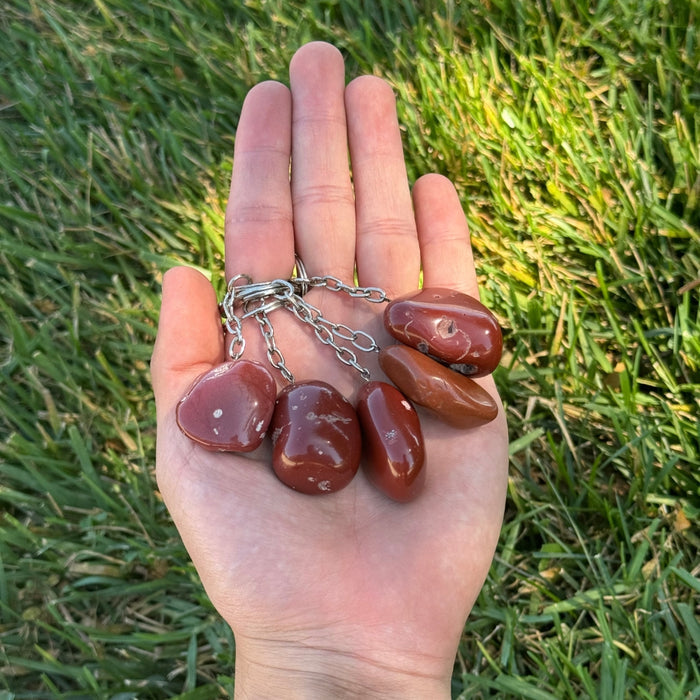 Hand holding Red Jasper keychains against a grass background