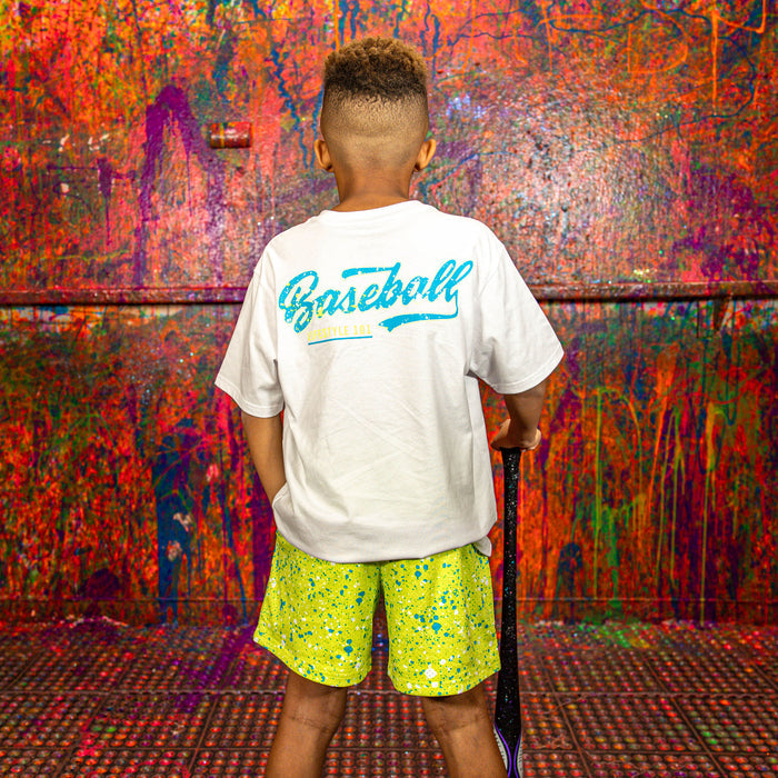Person wearing a white t-shirt with 'Baseball Lifestyle 101' text and yellow splattered shorts, standing in front of a multicolored wall.