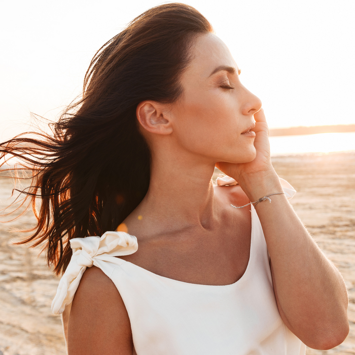 Woman with radiant skin enjoying sunset breeze, showcasing natural beauty and skincare results on beach