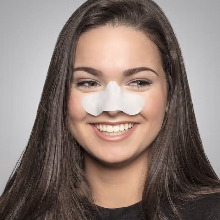 A smiling woman with long brown hair wears a STARSKIN SUNSET STRIPS white pore cleansing nose strip on her nose, standing against a plain gray background.